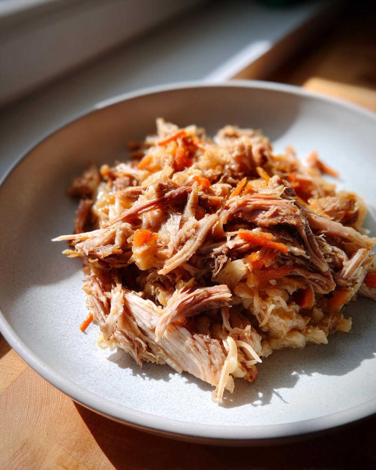 Close-up of tender shredded pork and sauerkraut mix served in a light-colored bowl.