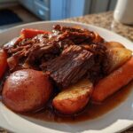 A plate of tender pot roast beef shredded and chunked, served with whole carrots and red potatoes in rich brown gravy.