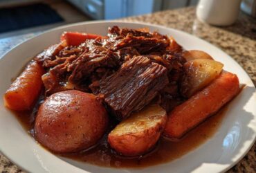A plate of tender pot roast beef shredded and chunked, served with whole carrots and red potatoes in rich brown gravy.