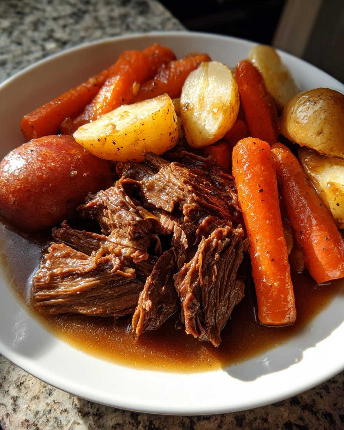 Shredded, tender pot roast served in rich gravy alongside cooked carrots and potatoes.