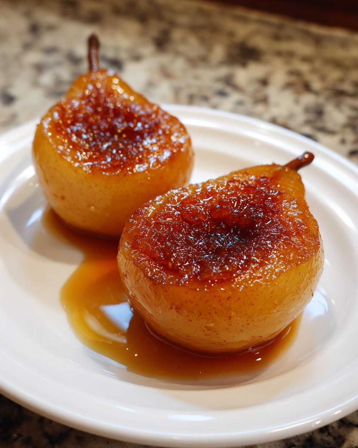 Two perfectly caramelized baked pears sitting in a pool of rich syrup on a white plate.