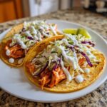 Close-up of two fully loaded salmon tacos topped with creamy white sauce and colorful slaw.