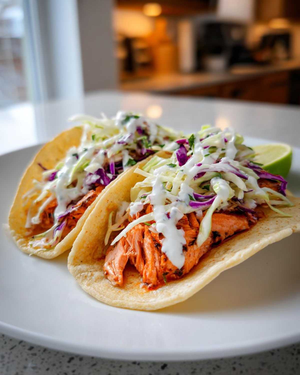 Two soft shell salmon tacos filled with flaky seasoned salmon, purple and white cabbage slaw, and drizzled with a white sauce.
