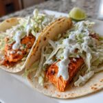 Two soft tortilla salmon tacos filled with seasoned salmon, shredded cabbage, and drizzled with a white creamy sauce.