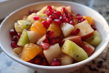 Close-up of a vibrant winter fruit salad featuring kiwi, orange segments, apple chunks, and bright pomegranate seeds.