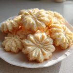 A pile of light, buttery whipped shortbread cookies shaped like flowers on a white plate.