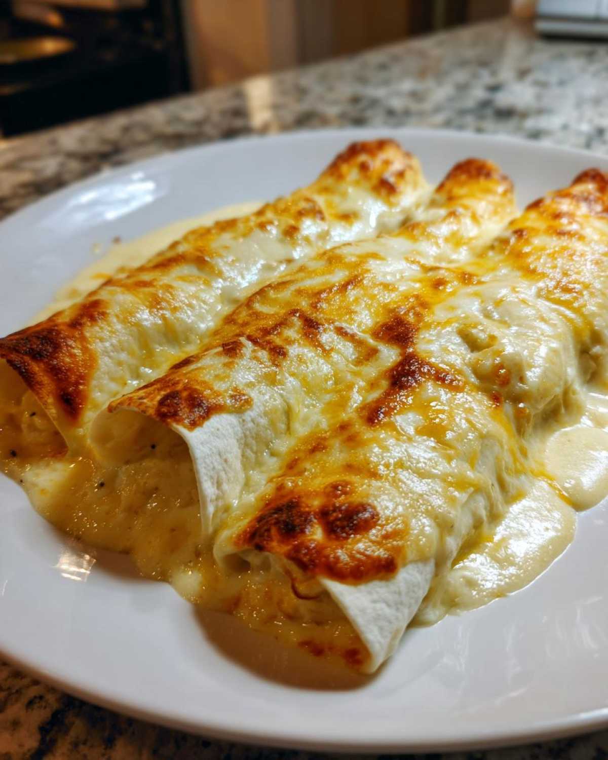 Three rolled white chicken enchiladas covered in melted, browned cheese sauce on a white plate.