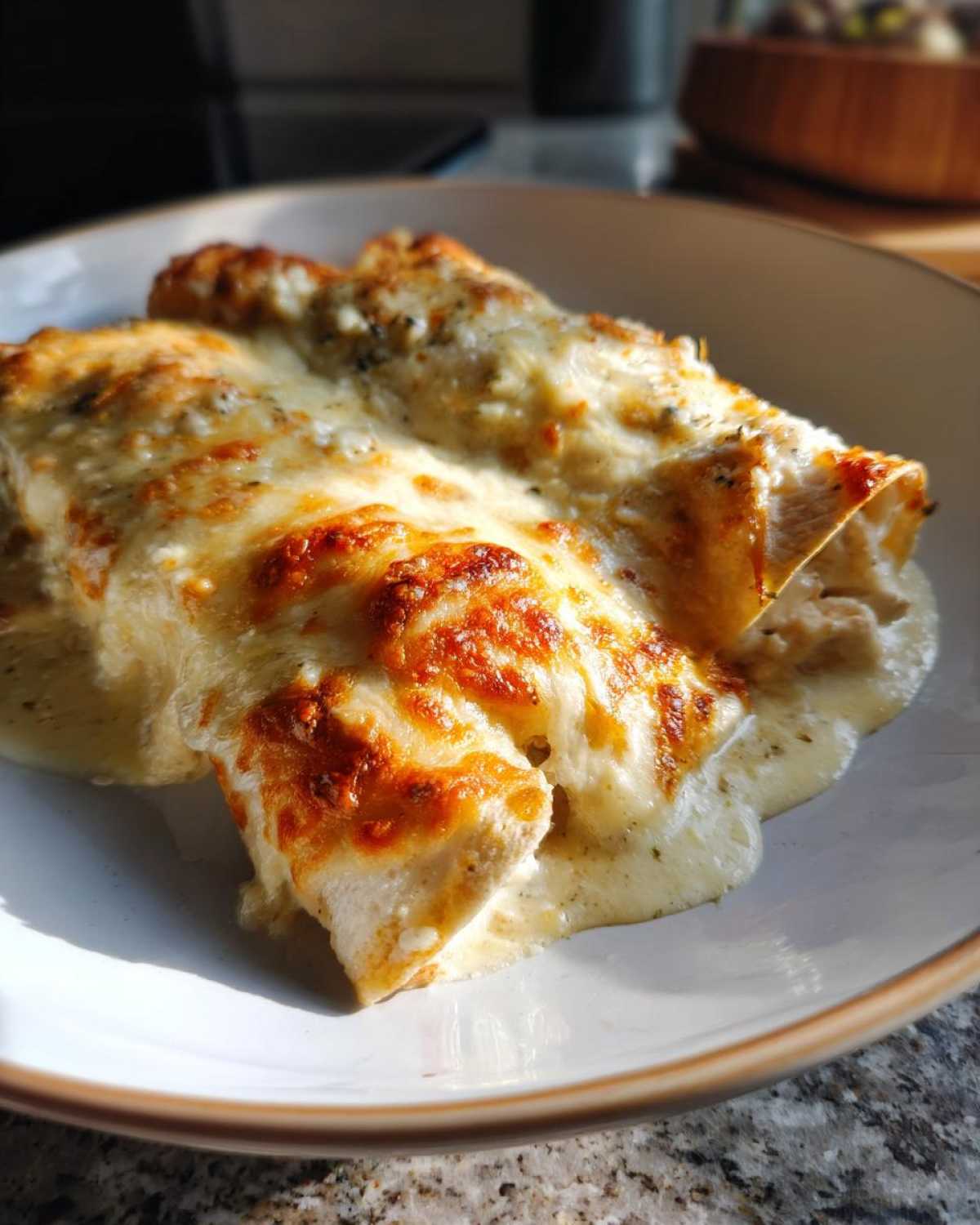 Close-up of two rich white chicken enchiladas covered in bubbling, browned cheese sauce.
