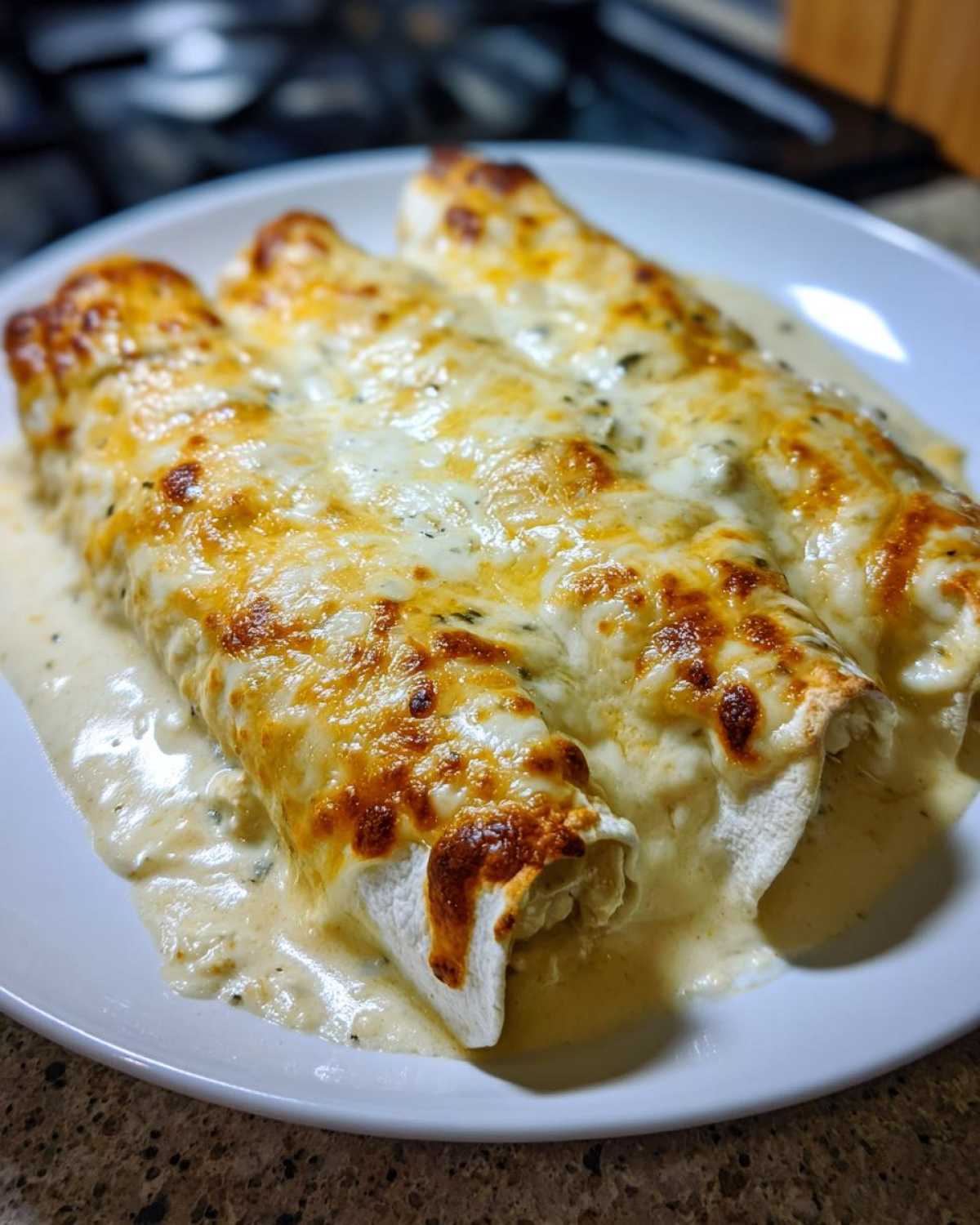 Three rolled white chicken enchiladas smothered in creamy sauce and topped with bubbly, browned cheese.