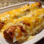 Close-up of baked white chicken enchiladas covered in melted, browned cheddar and white cheese.
