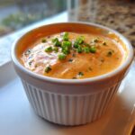 Close-up of creamy, orange-hued remoulade sauce topped with fresh green chives in a white ramekin.