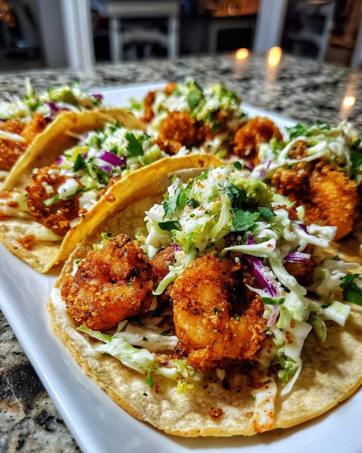 Close-up of several Air Fryer Crispy Garlic Shrimp Tacos loaded with slaw and seasoning on a white platter.