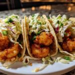 Three fully assembled Air Fryer Crispy Garlic Shrimp Tacos topped with fresh slaw and green onions on a white plate.