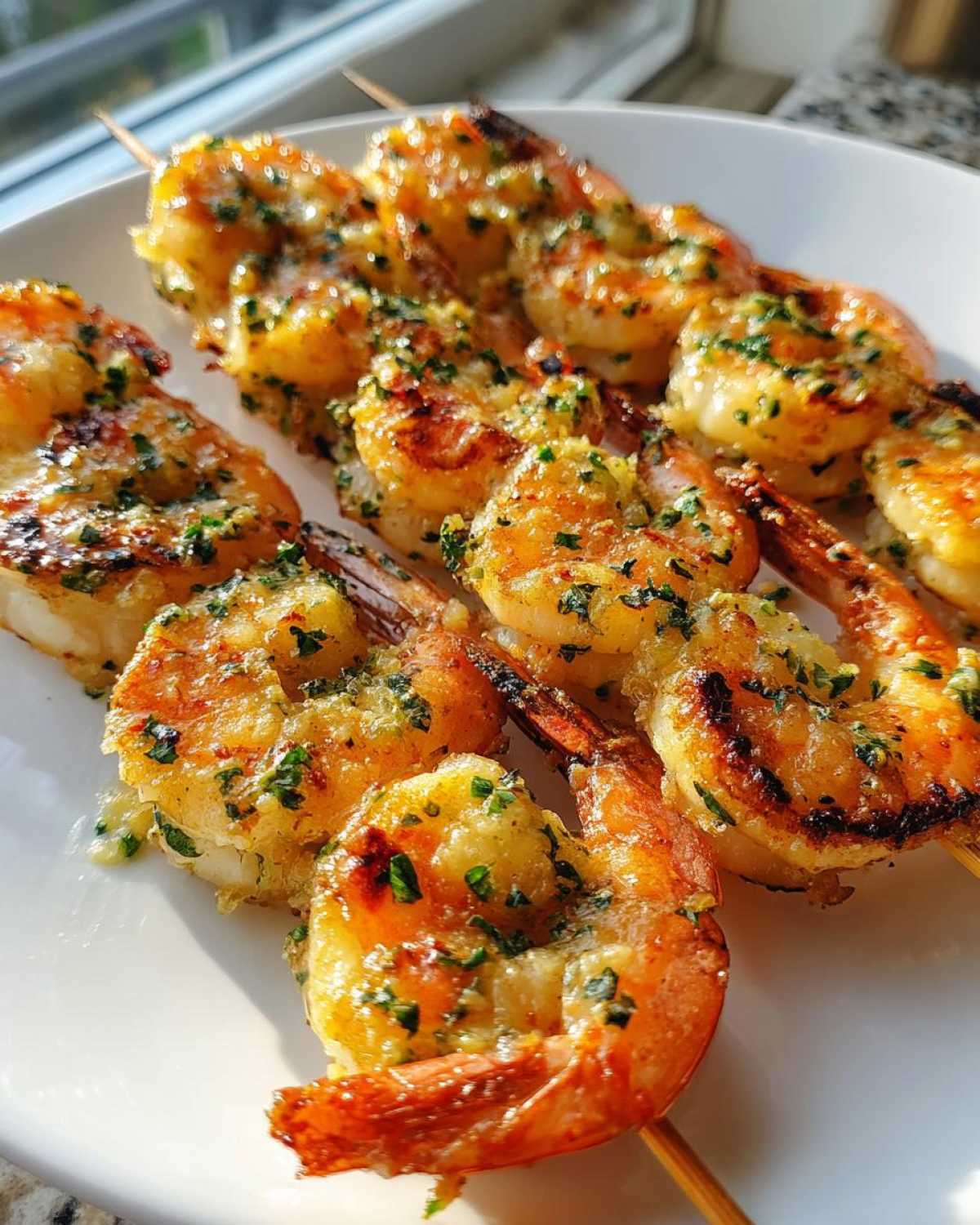 Close-up of golden, juicy Air Fryer Garlic Butter Shrimp Skewers coated in garlic and parsley, served on a white plate.