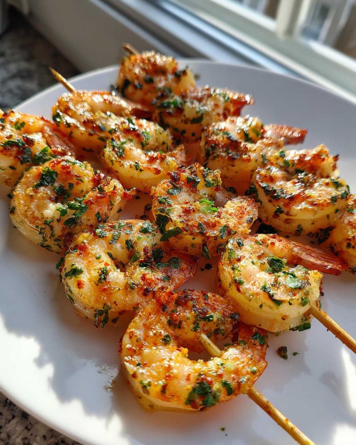 Close-up of golden Air Fryer Garlic Butter Shrimp Skewers seasoned with parsley and spices on a white plate.