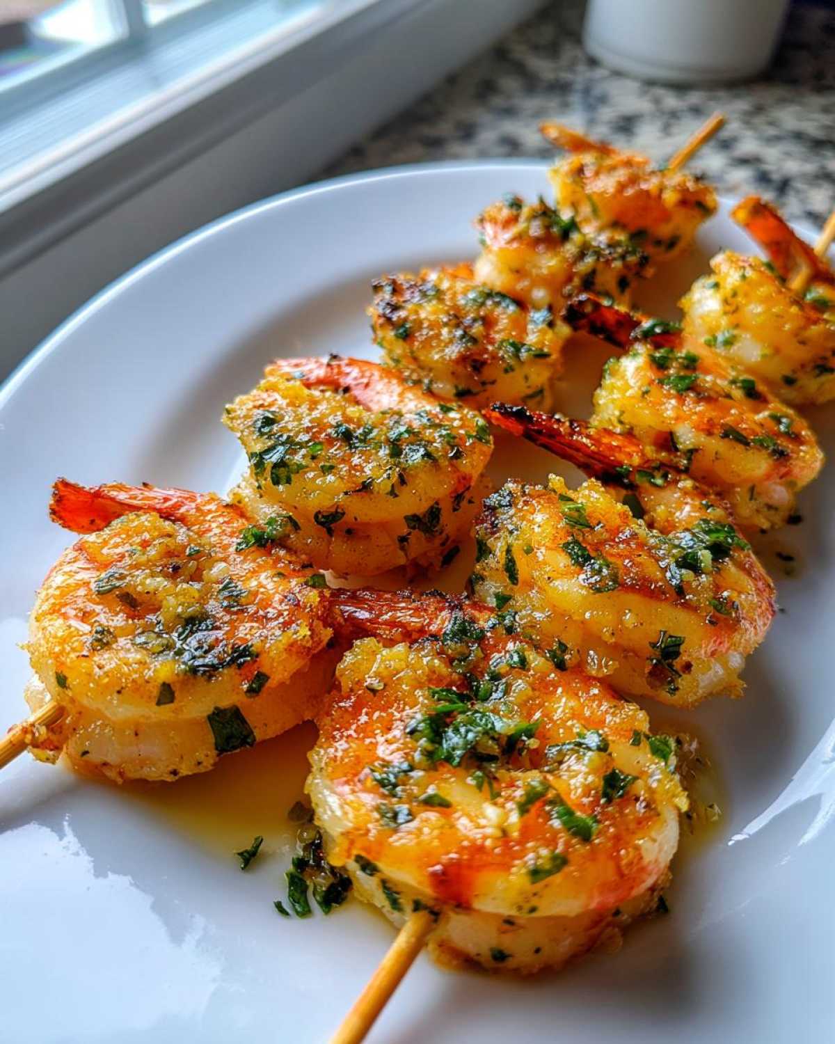 Close-up of several Air Fryer Garlic Butter Shrimp Skewers glistening with butter and parsley on a white plate.