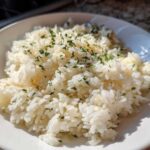 A close-up shot of fluffy white butter rice topped with chopped green parsley in a white bowl.