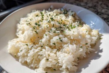 A close-up shot of fluffy white butter rice topped with chopped green parsley in a white bowl.