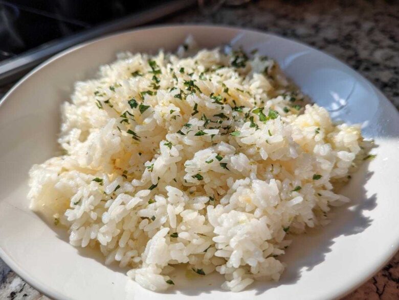 A close-up shot of fluffy white butter rice topped with chopped green parsley in a white bowl.