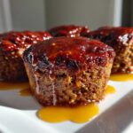 Four perfectly shaped mini meatloaf muffins topped with a thick, glossy red glaze, sitting on a white plate.