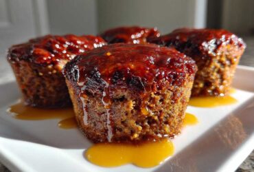 Four perfectly shaped mini meatloaf muffins topped with a thick, glossy red glaze, sitting on a white plate.