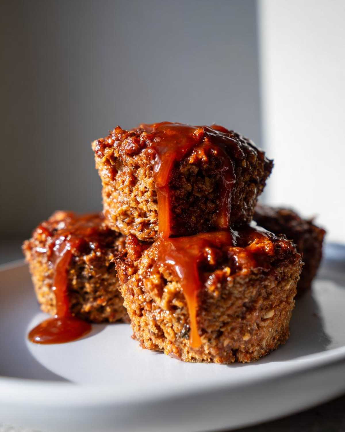 Close-up of stacked mini meatloaf muffins generously topped with a thick, dripping brown glaze.