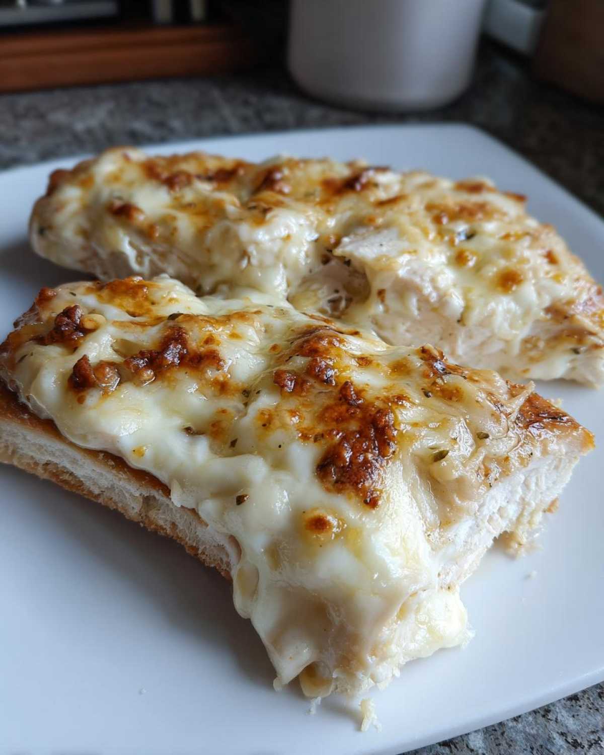 Two pieces of juicy baked ranch chicken topped with melted, browned cheese served on bread.