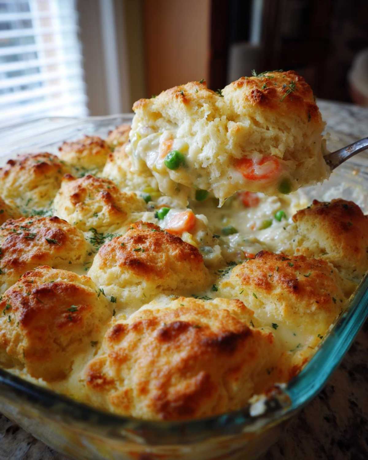 A spoonful of creamy chicken pot pie casserole filling and a golden biscuit being lifted from the baking dish.