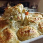 A spoonful of creamy chicken pot pie casserole filling with vegetables being lifted above the baking dish.