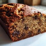 A close-up, cross-section view of a moist chocolate chip vegan banana bread loaf with a golden-brown crust.