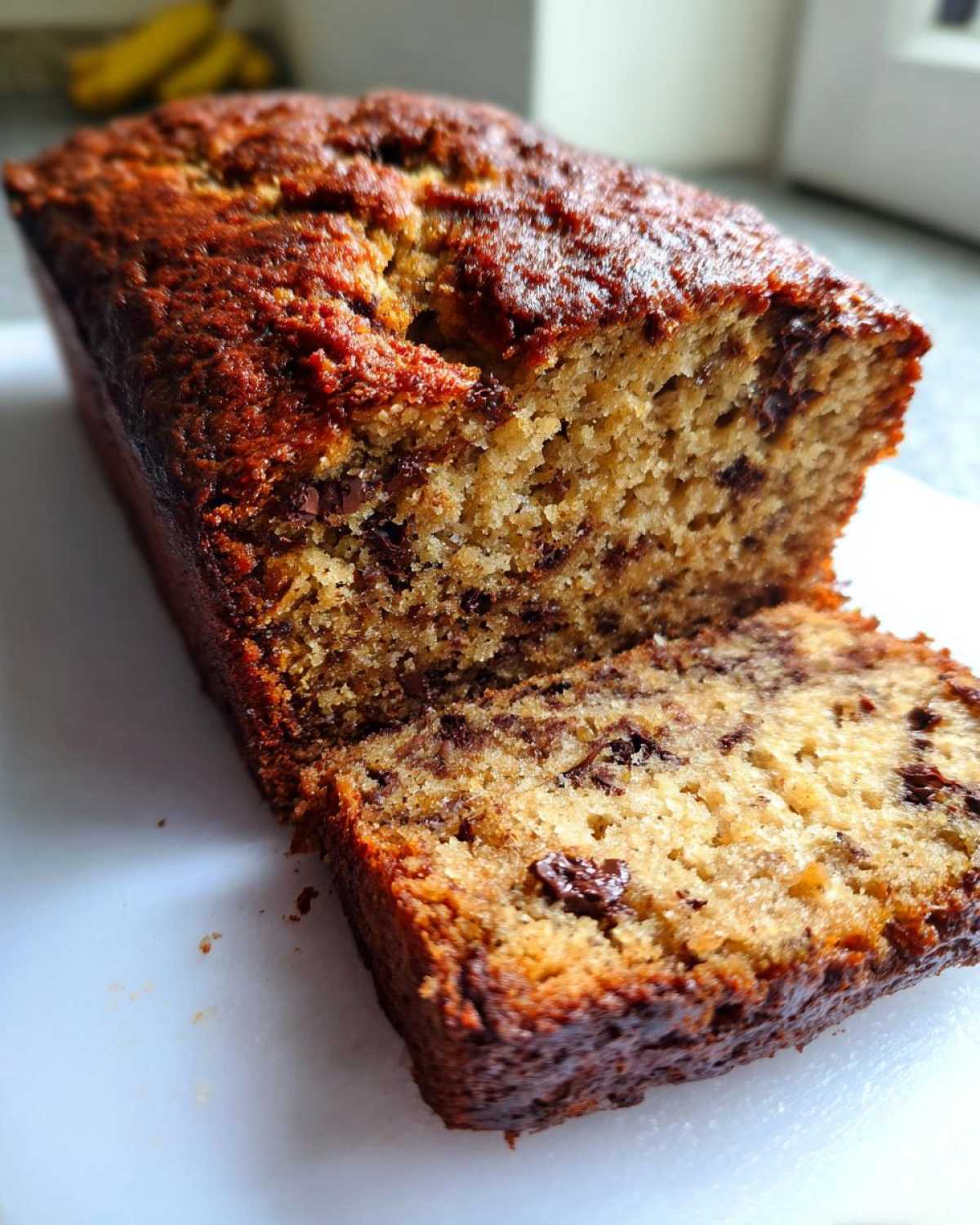 A moist, sliced loaf of chocolate chip vegan banana bread showing a rich, dark crust and soft interior.