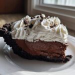 A decadent slice of chocolate mousse pie featuring a dark crust, rich filling, and topped with whipped cream and chocolate shavings.