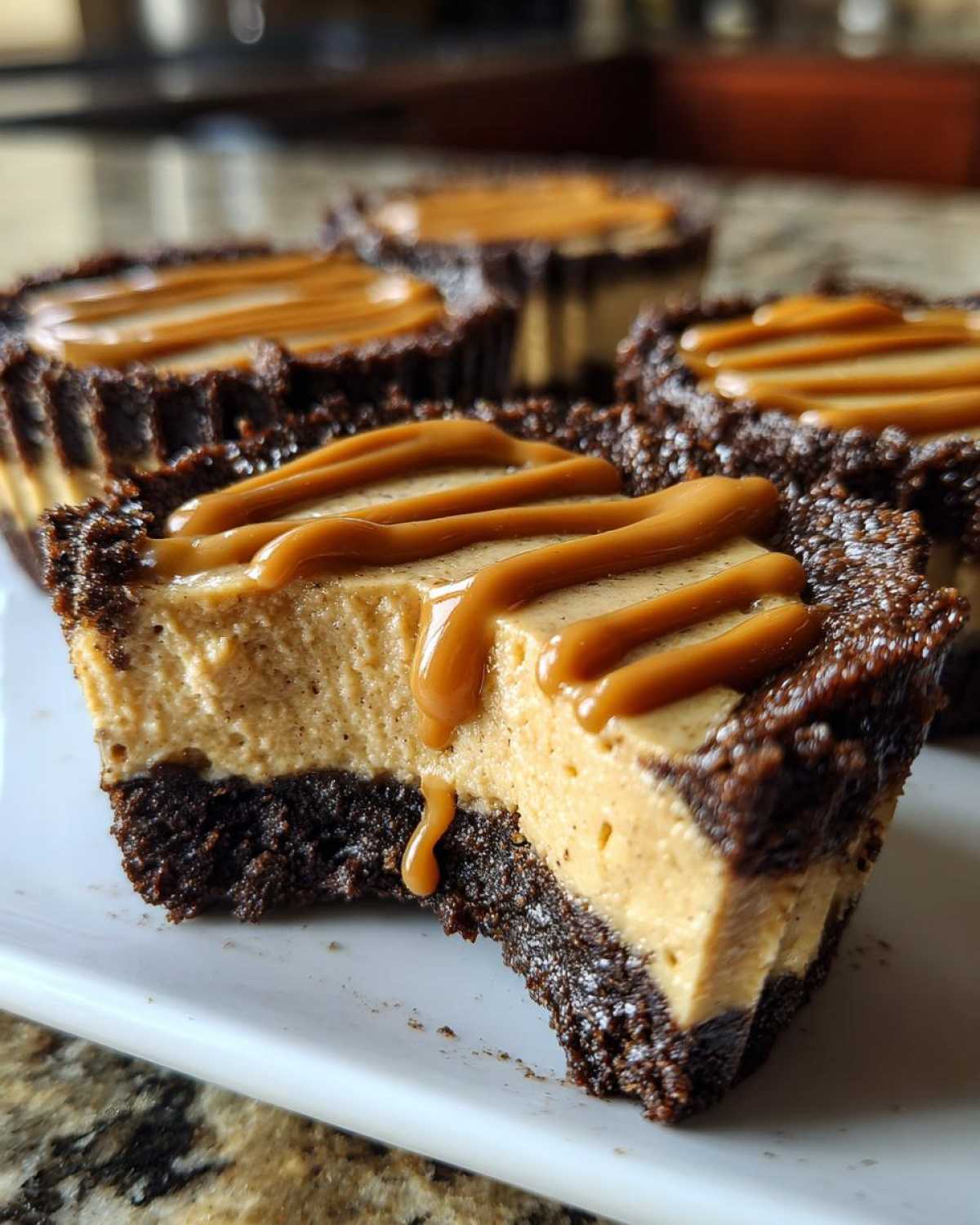 A cross-section of a cookie butter cheesecake cup showing the dark crust and creamy filling, topped with a caramel drizzle.