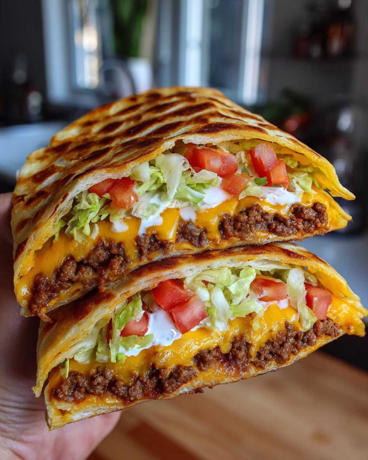 Two halves of a grilled Copycat Taco Bell Crunchwrap Supreme showing layers of seasoned beef, melted cheese, lettuce, tomatoes, and sour cream.