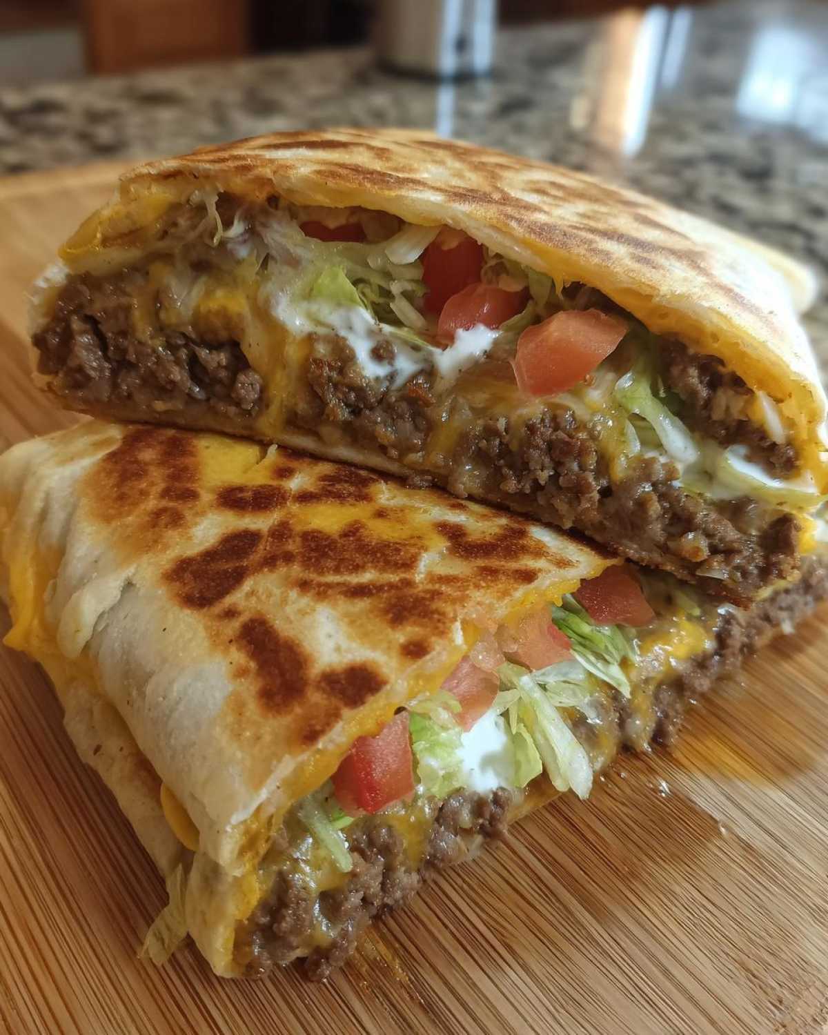 Close-up of a Copycat Taco Bell Crunchwrap Supreme cut in half, showing seasoned beef, cheese, lettuce, tomato, and sour cream.