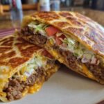 A Copycat Taco Bell Crunchwrap Supreme cut in half, showing seasoned beef, cheese, lettuce, tomato, and sour cream.