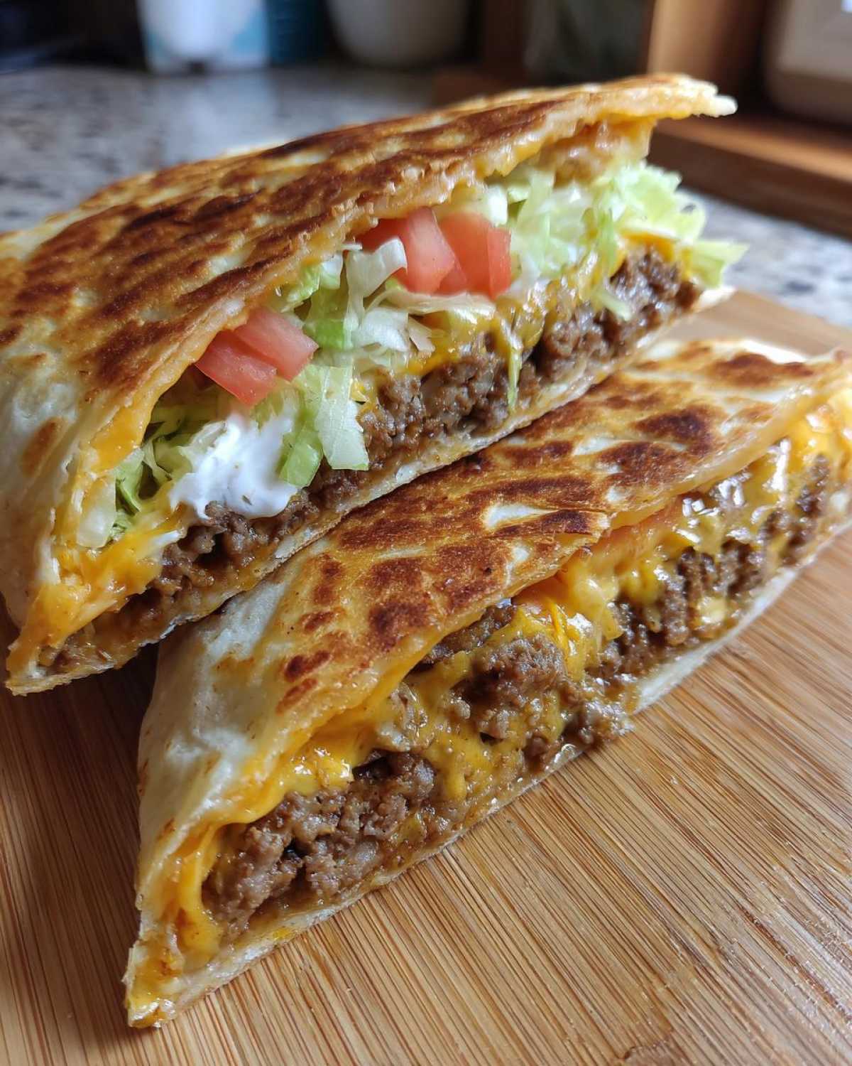 Two halves of a golden-brown Copycat Taco Bell Crunchwrap Supreme showing seasoned beef, melted cheese, lettuce, tomato, and sour cream.