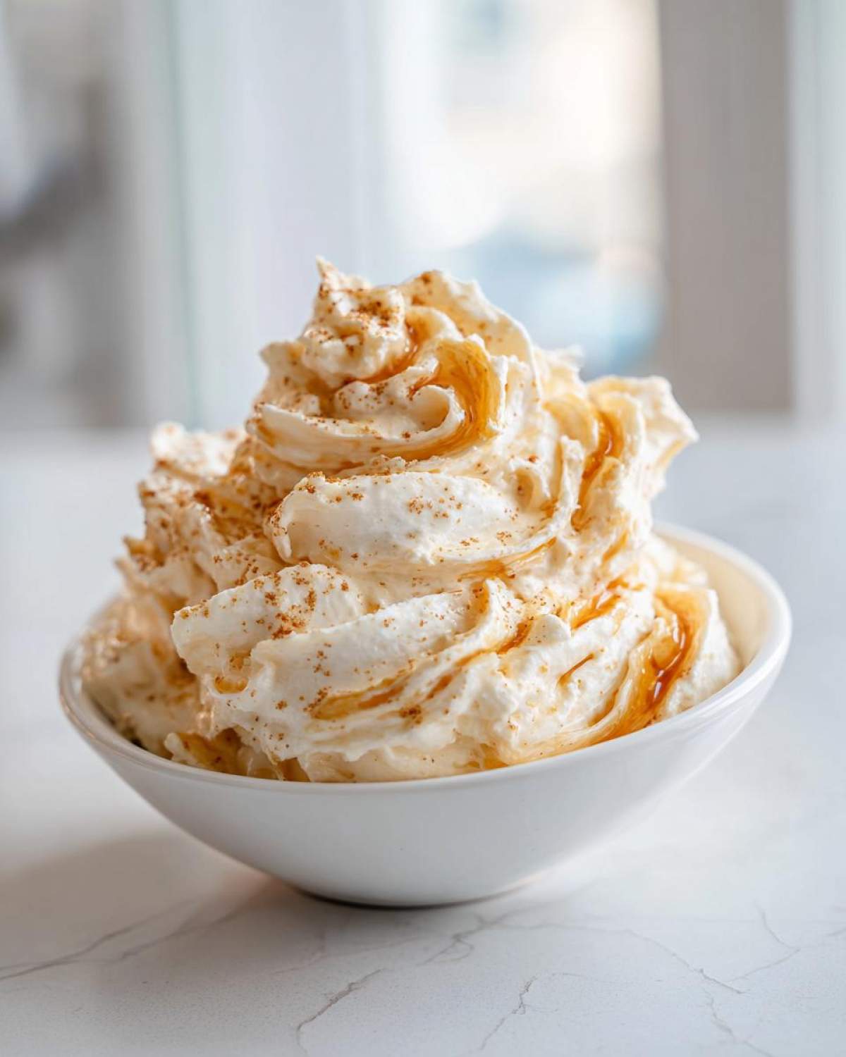 A bowl filled with fluffy Copycat Texas Roadhouse Cinnamon Honey Butter, drizzled with honey and sprinkled with cinnamon.