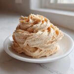 A swirl of whipped Copycat Texas Roadhouse Cinnamon Honey Butter dusted with cinnamon on a small white plate.