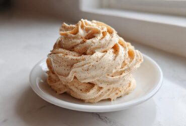 A swirl of whipped Copycat Texas Roadhouse Cinnamon Honey Butter dusted with cinnamon on a small white plate.