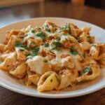 A close-up of creamy chicken enchilada pasta topped with melted cheese and fresh parsley on a white plate.