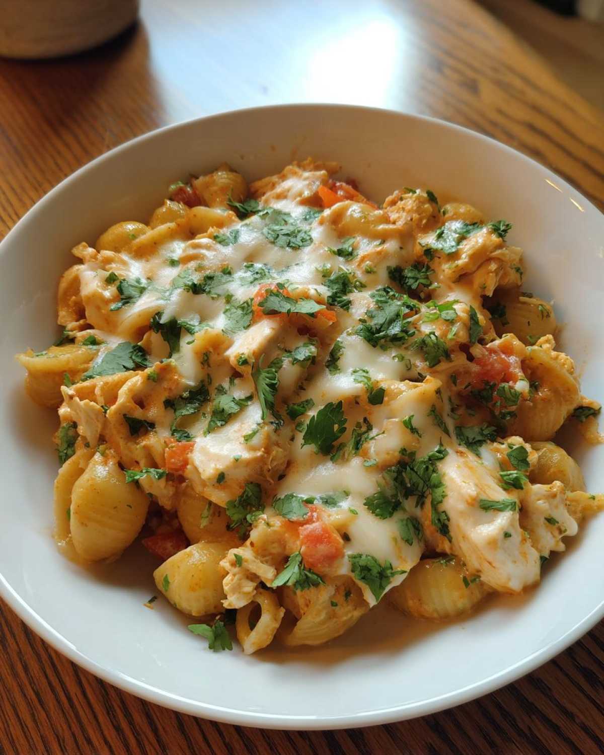 A close-up of creamy chicken enchilada pasta with melted cheese and fresh cilantro in a white bowl.