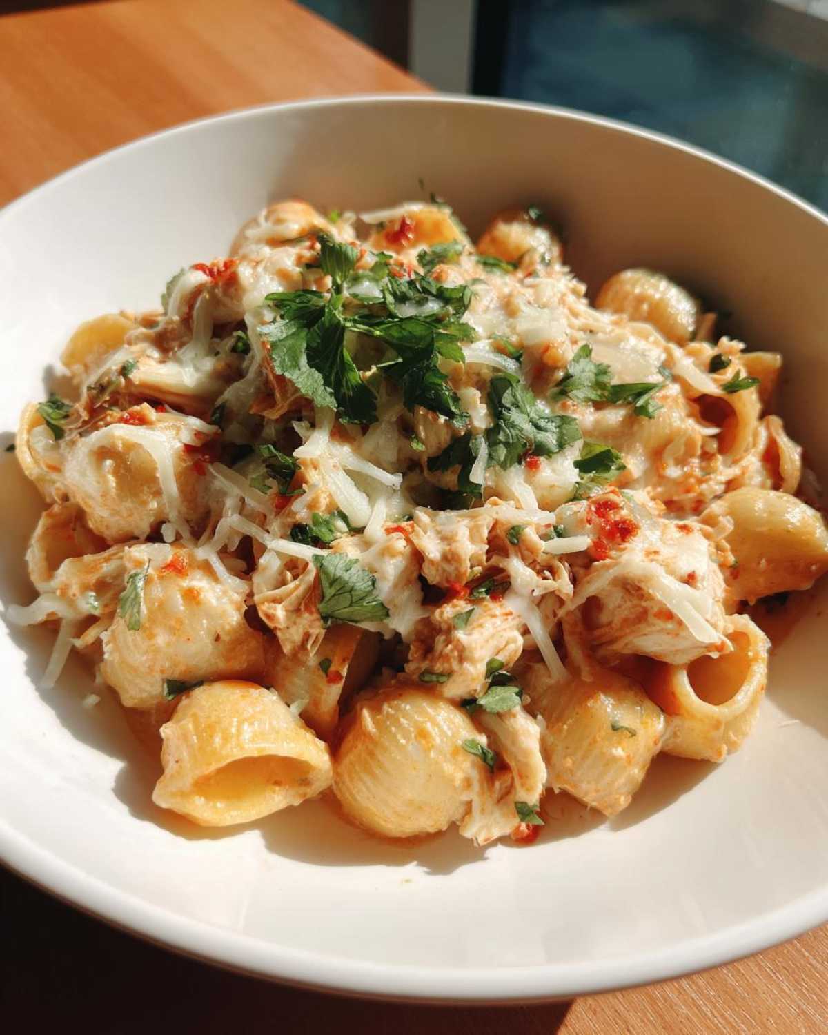 Close-up of creamy chicken enchilada pasta made with shells, topped with shredded cheese and fresh parsley.
