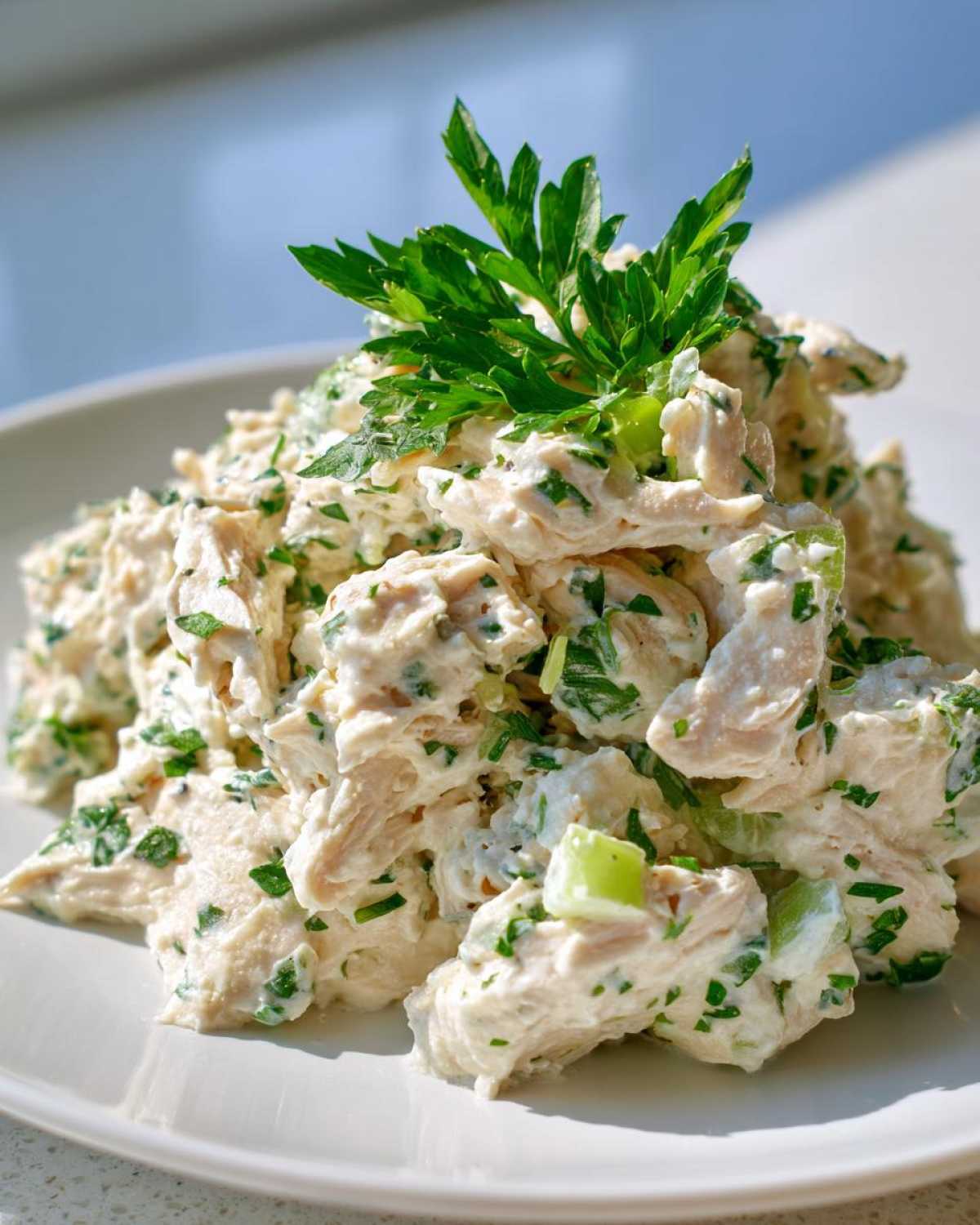A mound of creamy greek yogurt chicken salad mixed with herbs and celery, topped with fresh parsley.