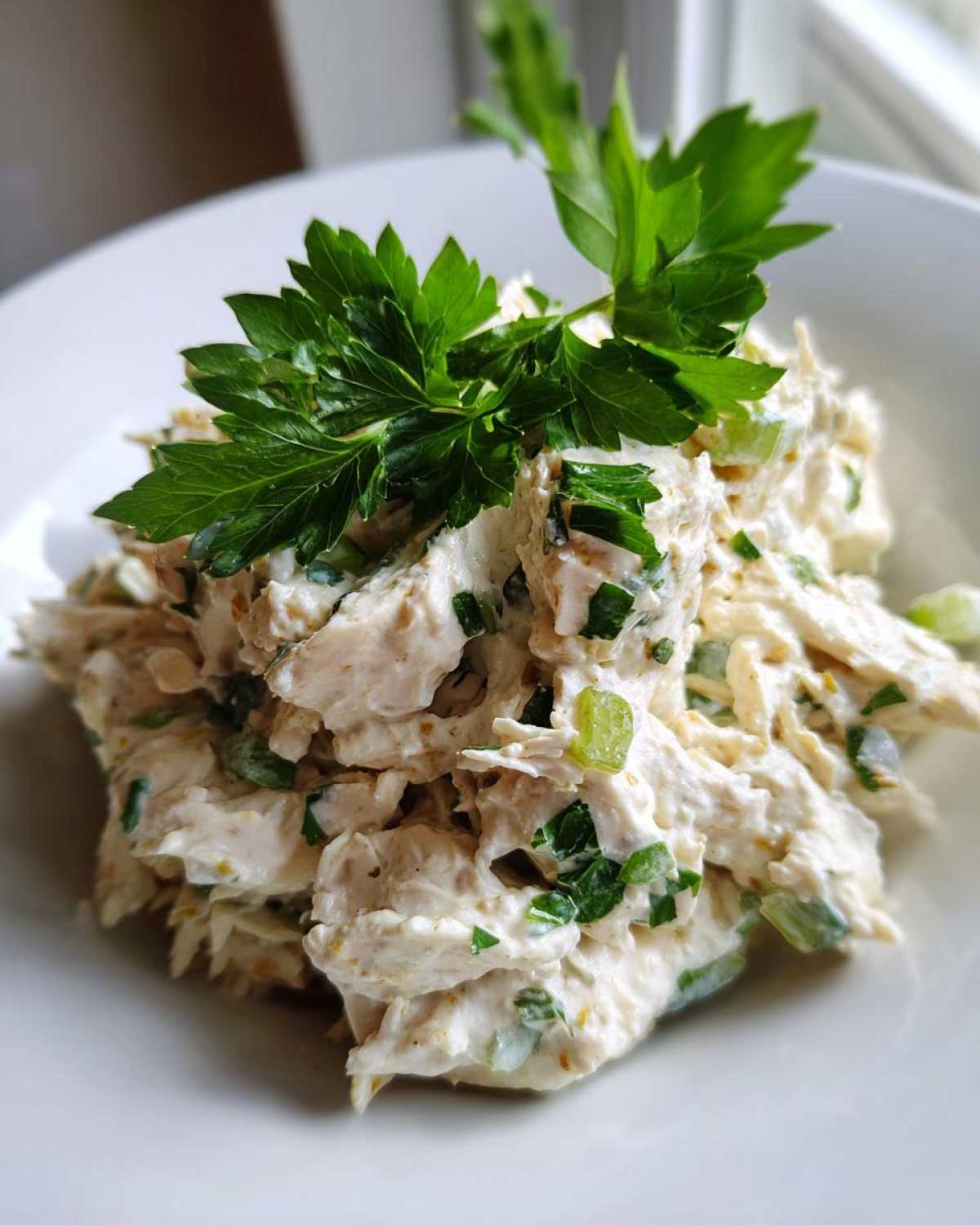 A close-up of creamy greek yogurt chicken salad mixed with green onions and topped with fresh parsley.