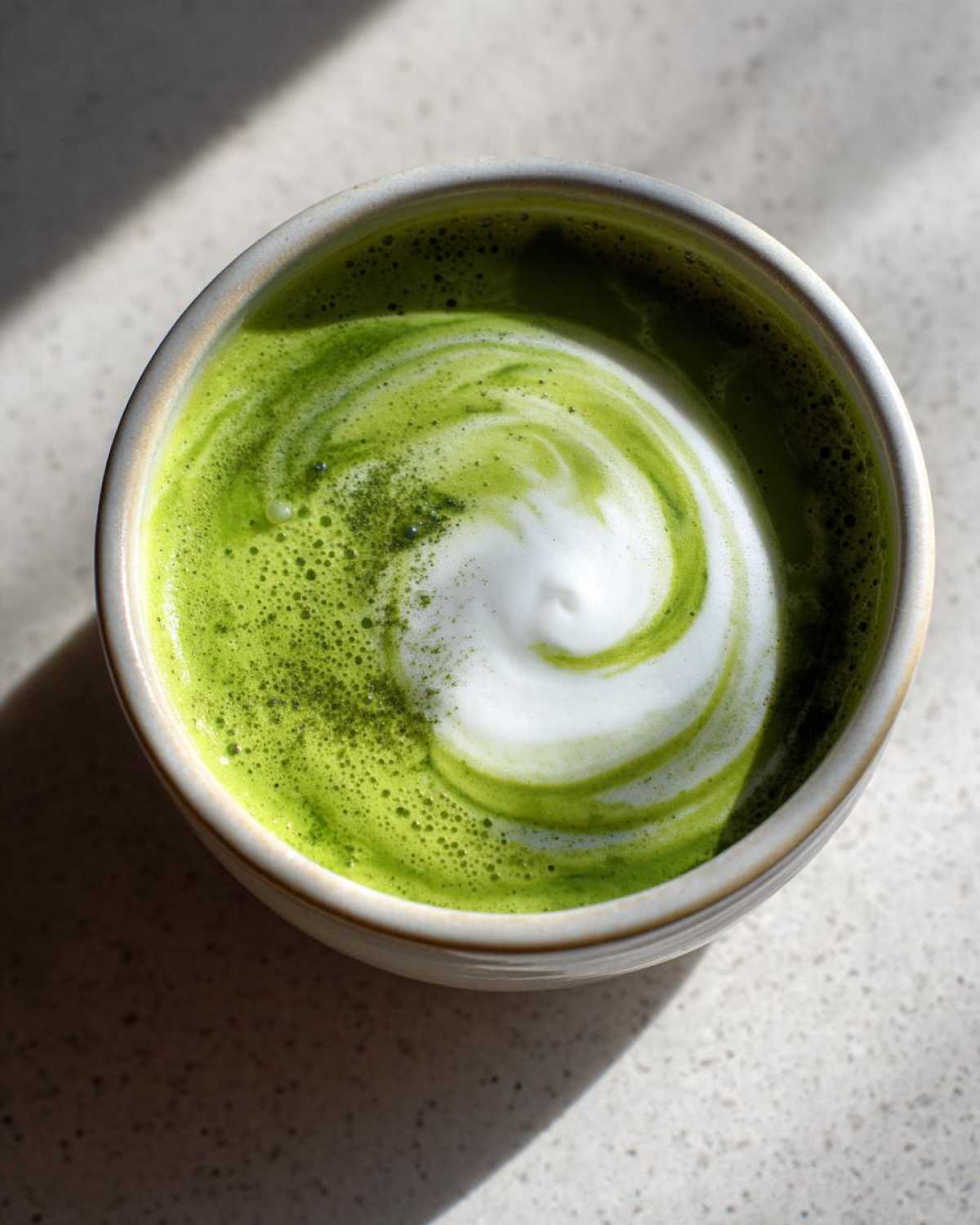 Overhead view of a vibrant green drink with a white, foamy swirl, resembling Instant Pot Creamy Asparagus Soup.