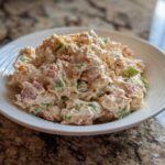 A close-up of a creamy ham salad recipe served in a white bowl on a granite countertop.