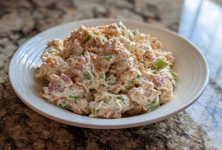 A close-up of a creamy ham salad recipe served in a white bowl on a granite countertop.