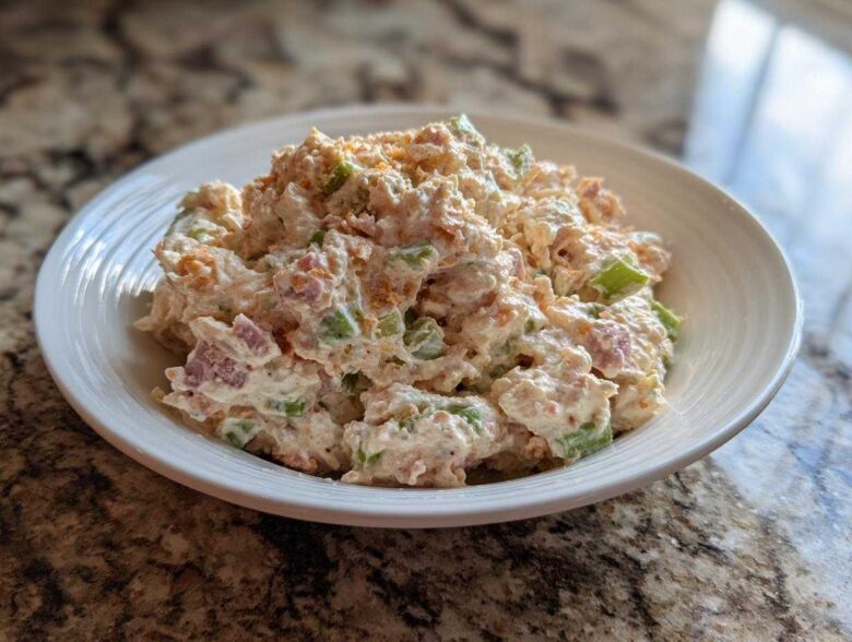 A close-up of a creamy ham salad recipe served in a white bowl on a granite countertop.