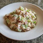 A close-up of a creamy ham salad recipe mixed with diced green celery, served in a white bowl.